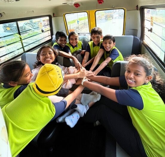Children reaching in to put their hands together in the middle of the bus, smiling.
