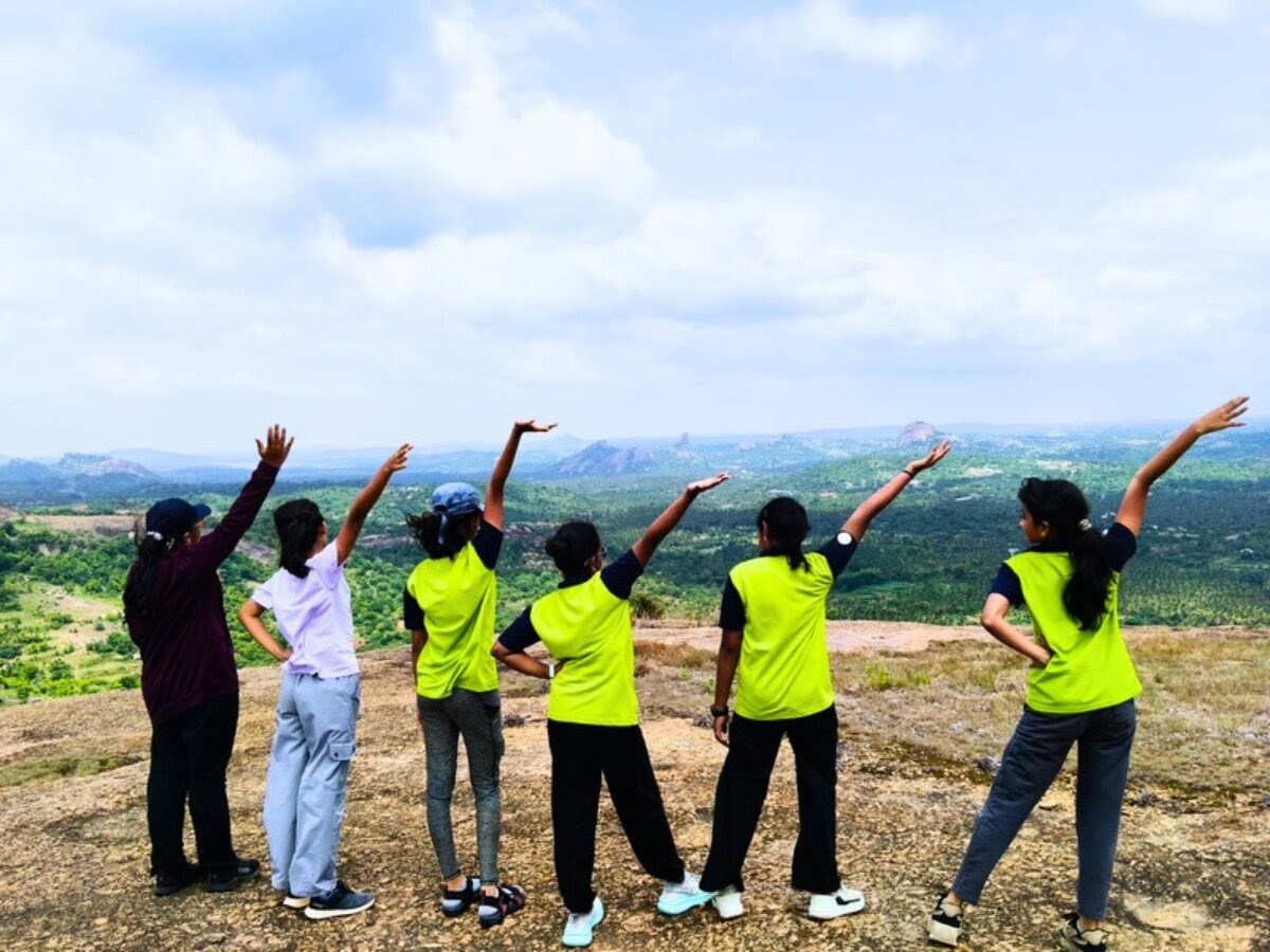 Children standing on the summit with their arms raised towards an open, cloud-filled sky.